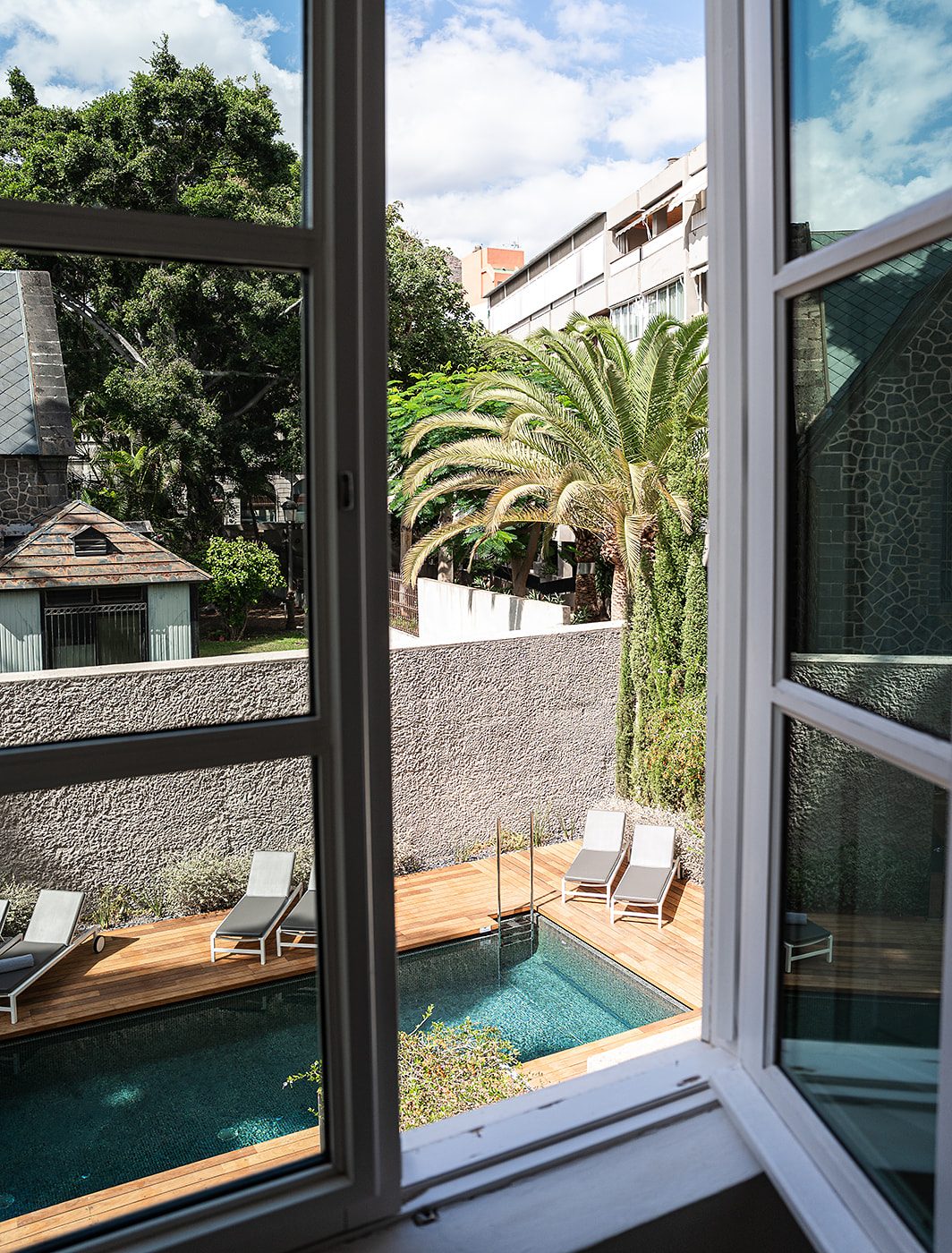 An original 19th-century white wooden window, left slightly ajar, offering views of the swimming pool from Suite 3 at The Park Suites